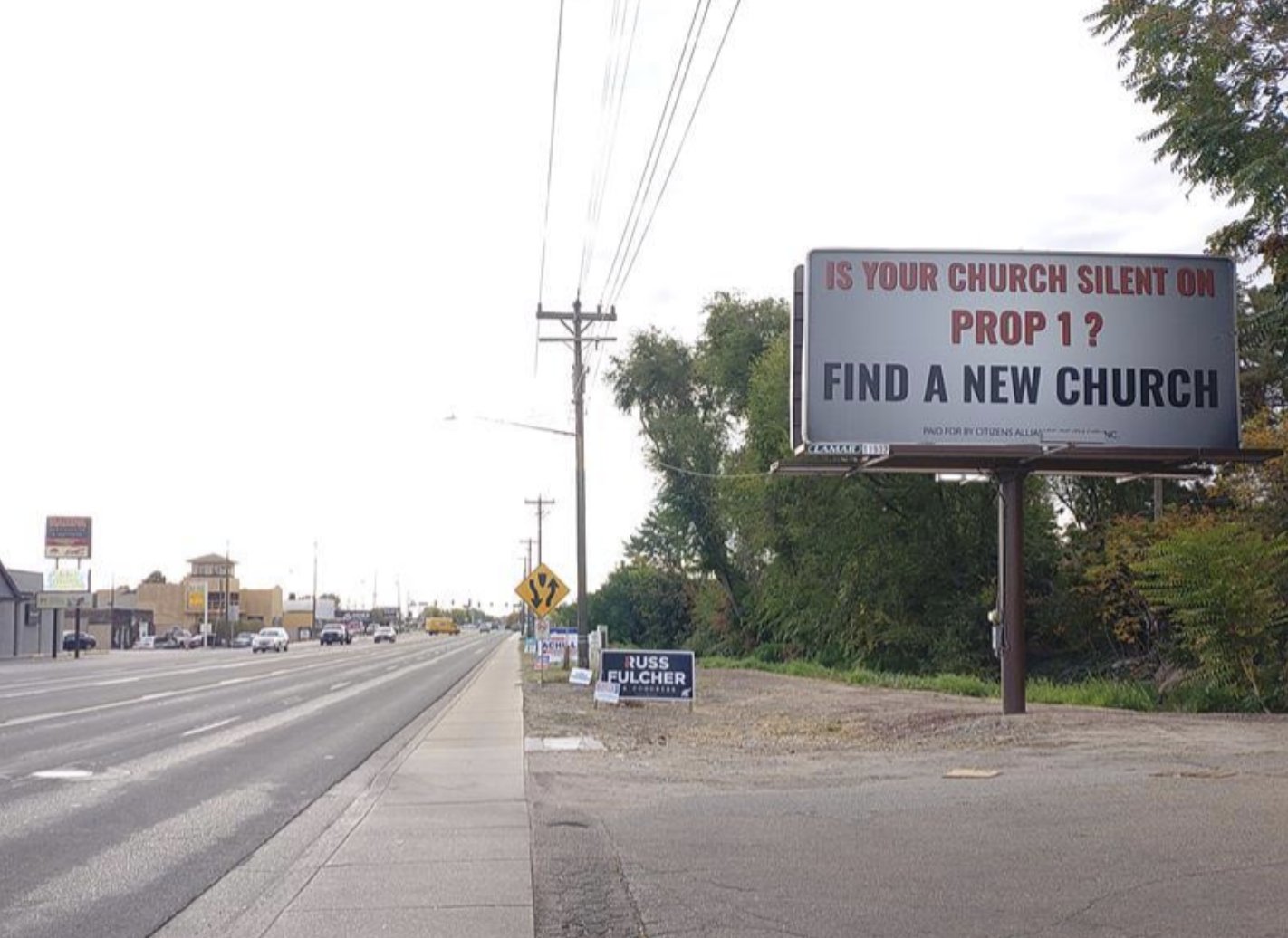 A roadside billboard reading Is Your Church Silent on Prop 1? Find a New Church, beside a state highway